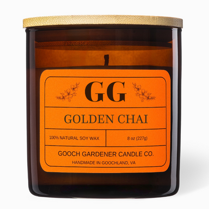 An amber glass jar candle with a light wood lid and a bright orange label reading &