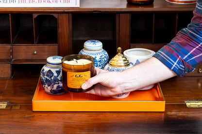 Person holding a candle with a visible brand label on a wooden surface with decorative items.