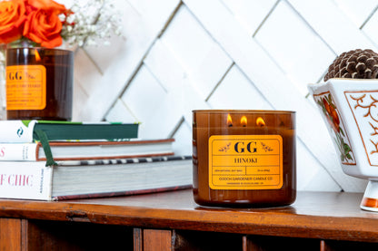 GG Hinoki candle on a wooden surface with books and decorative items in the background