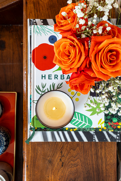 Book titled 'Herbal' with a candle and flowers on a wooden surface
