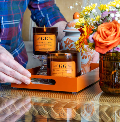 Candle with 'GG' branding on a table with flowers and a person in a plaid shirt.