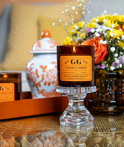 Candle labeled 'GG Golden Amber' on a table with decorative items in the background