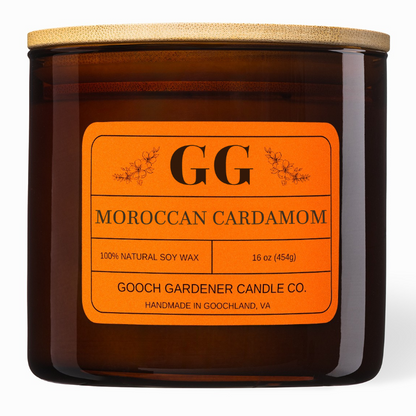 An amber glass jar candle with a light wood lid and a bright orange label reading &