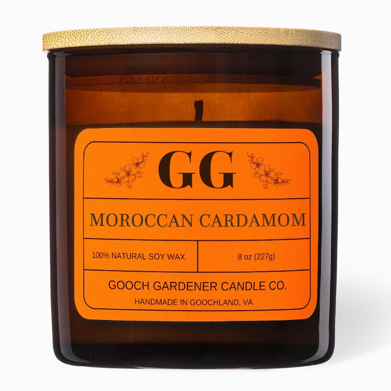 An amber glass jar candle with a light wood lid and a bright orange label reading &